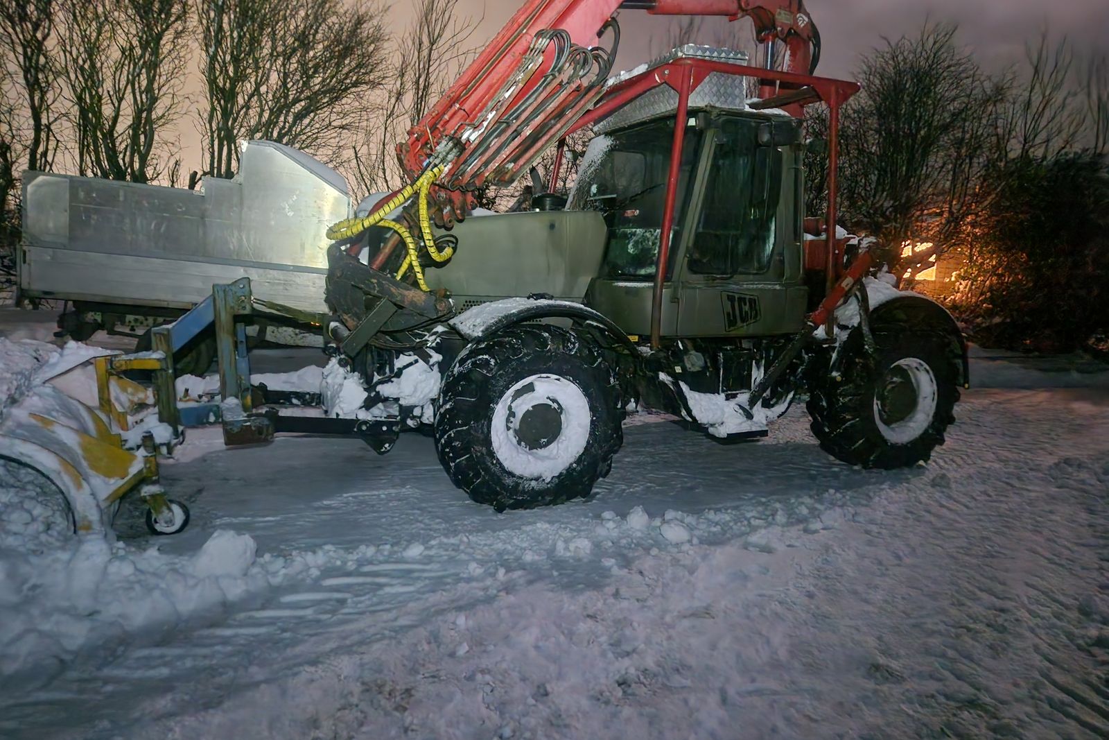 Tractor-mounted plough clearing a yard at dusk